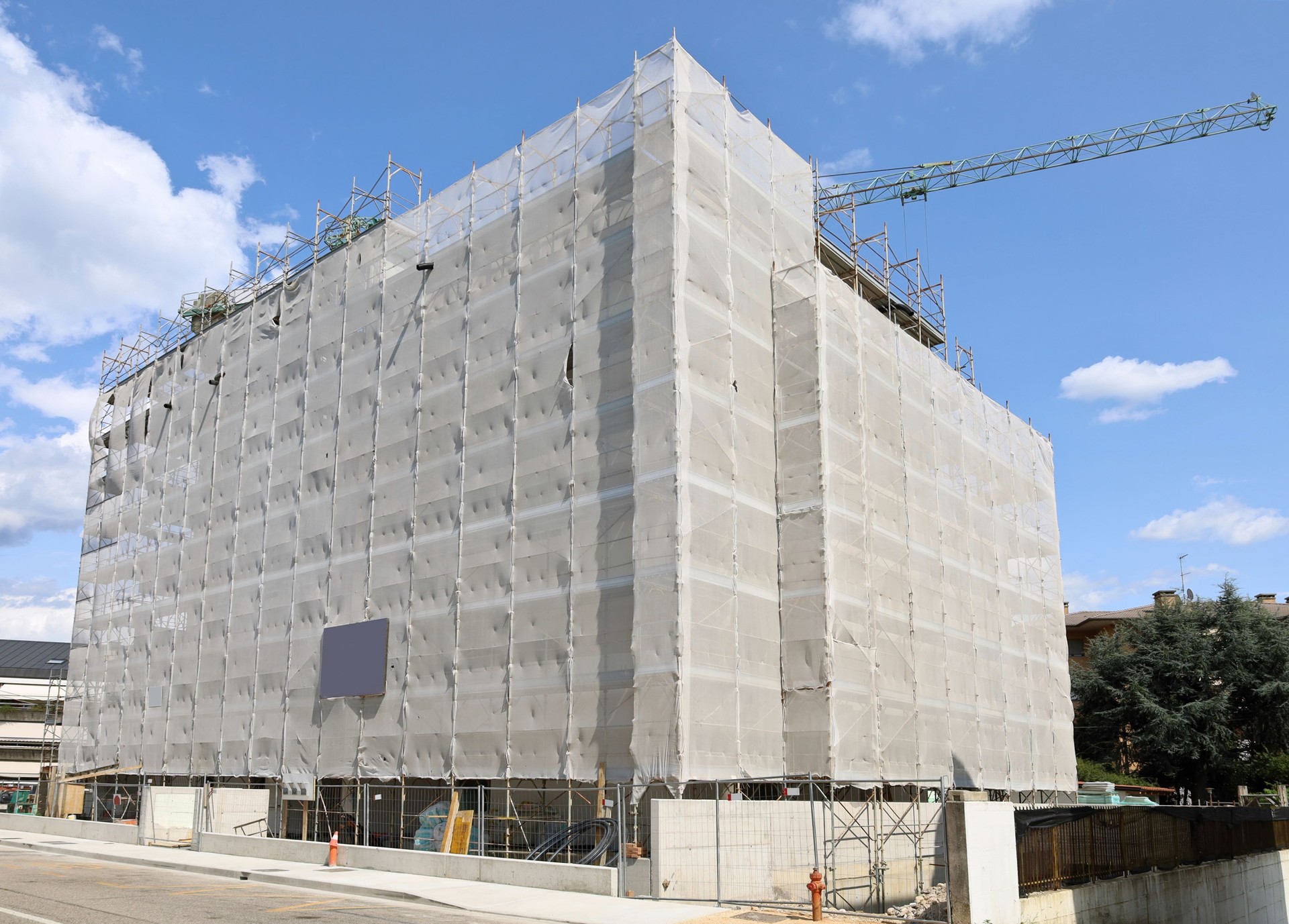 Grand bâtiment en cours de rénovation entièrement recouvert de feuilles de plastique de construction sur les échafaudages