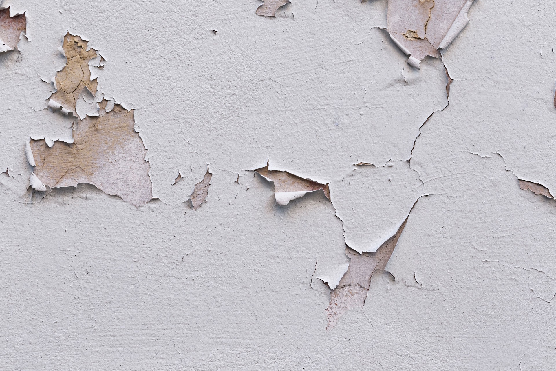 Gros plan d’un mur de façade mal fixé recouvert de fissures dans le stuc et la peinture.