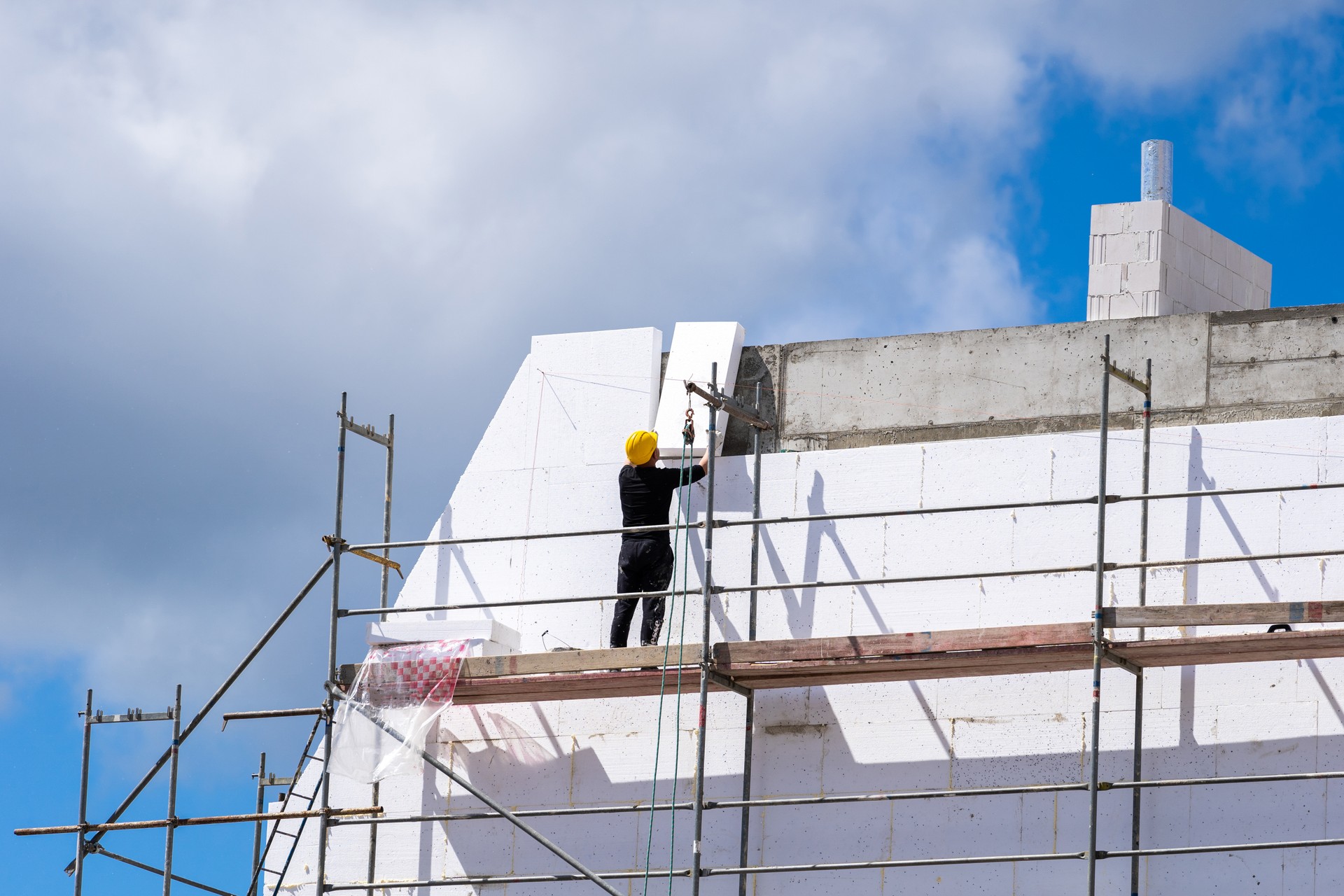 Un homme installe des feuilles de polystyrène sur le mur de la façade de la maison pour la protection thermique